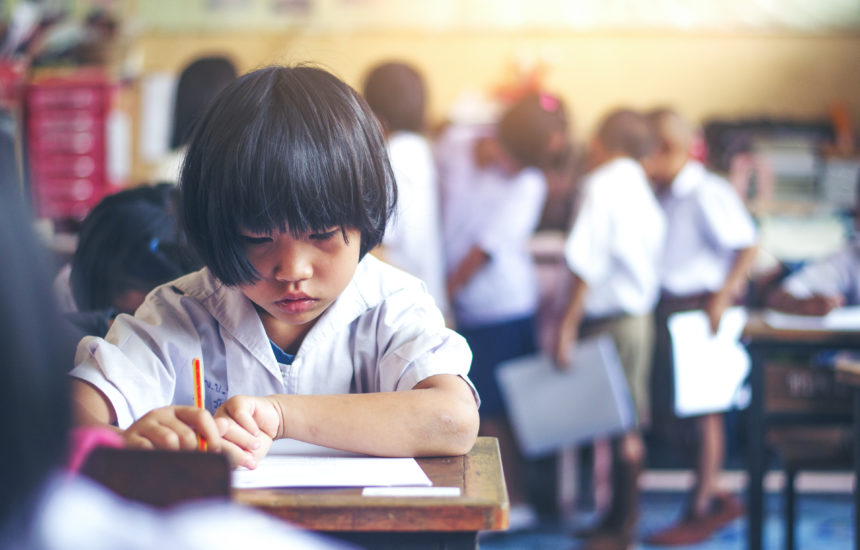 A young girl at a school desk writing.