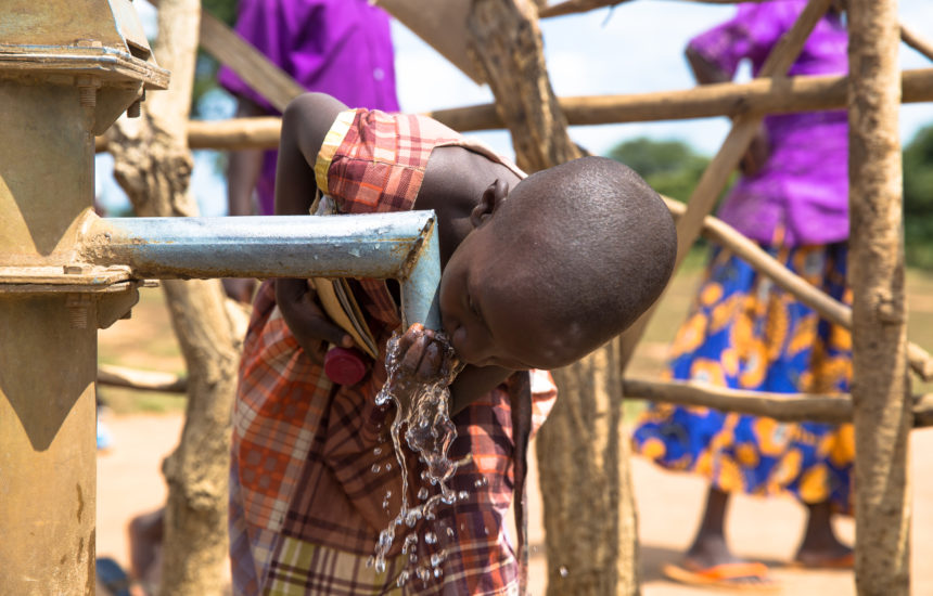 A young girl drinking water from a spout outside.