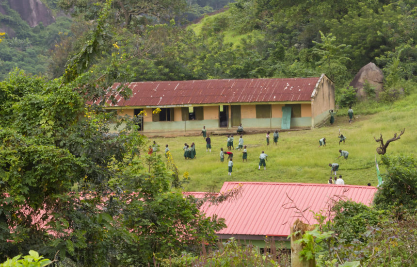 A wide shot photo of a building outside with multiple people in the grass surrounding it.