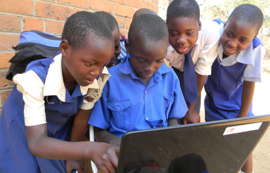 A group of kids working on a laptop outside.