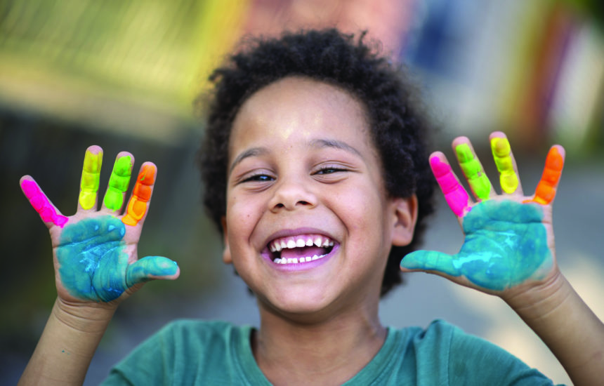 A young boy smiling with different colored paint on his hands