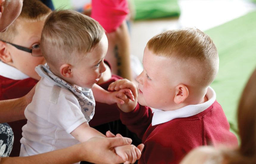 A young boy holds a baby's hands and looks at him