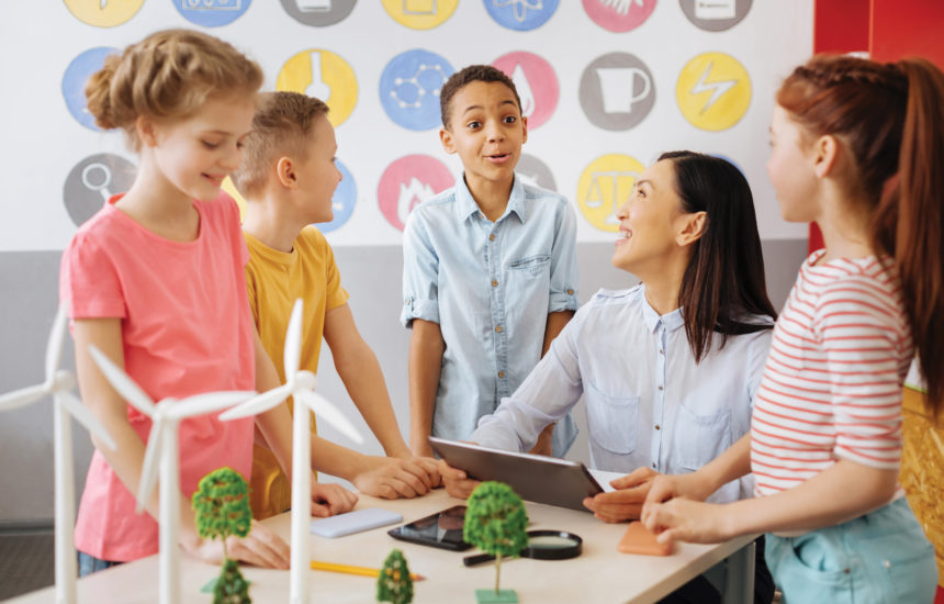 A woman is working with a group of students, smiling