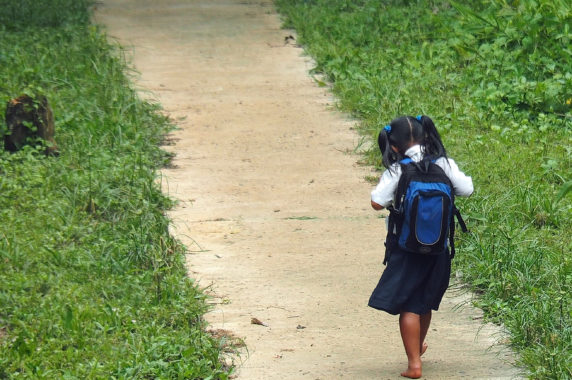 A girl wears a backpack and walks to school barefoot