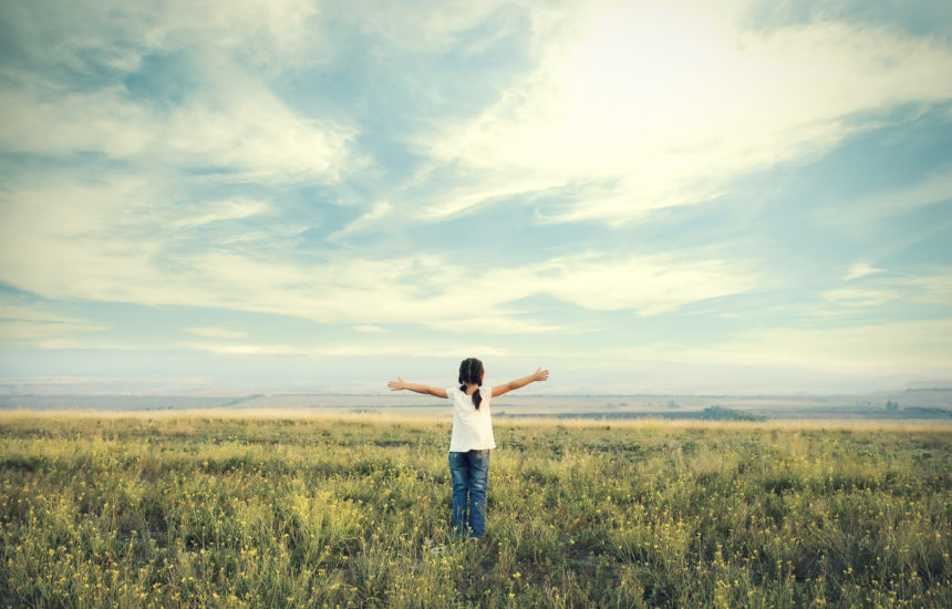 A girl holds her hands out in a meadow