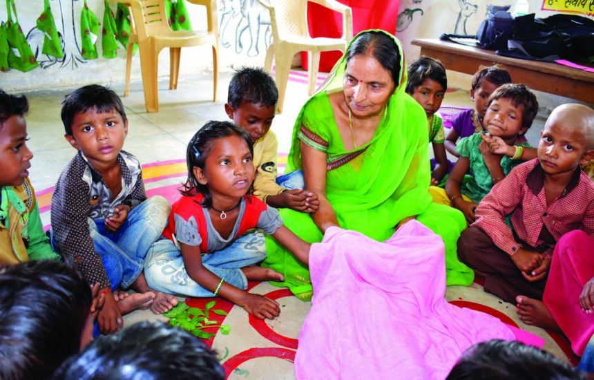 One woman sitting in a circle with young children sitting all around her.