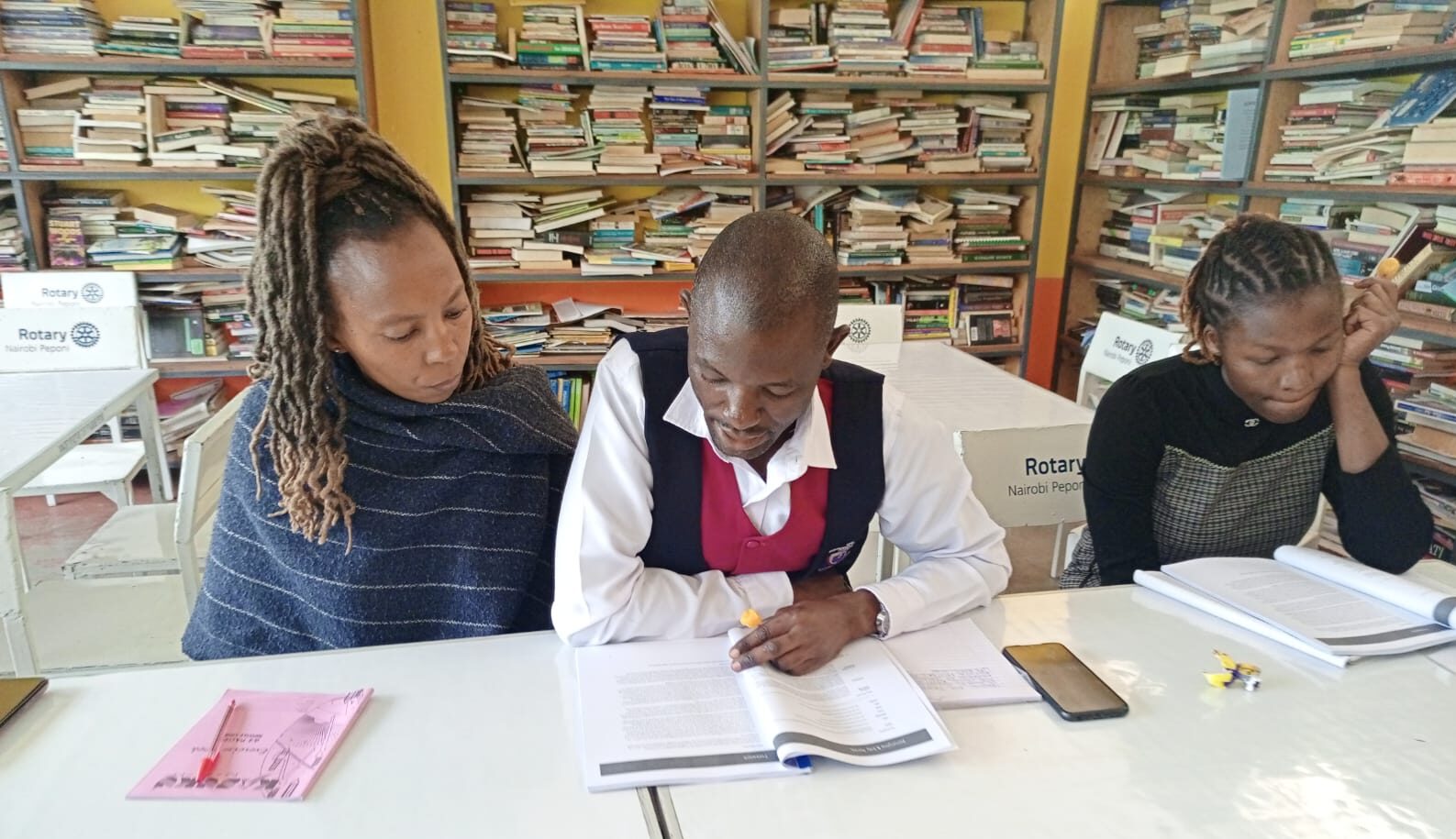 Three people looking at booklets while sitting at a shared desk