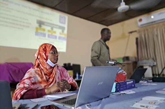 Woman at a computer with a man with a presentation in the background