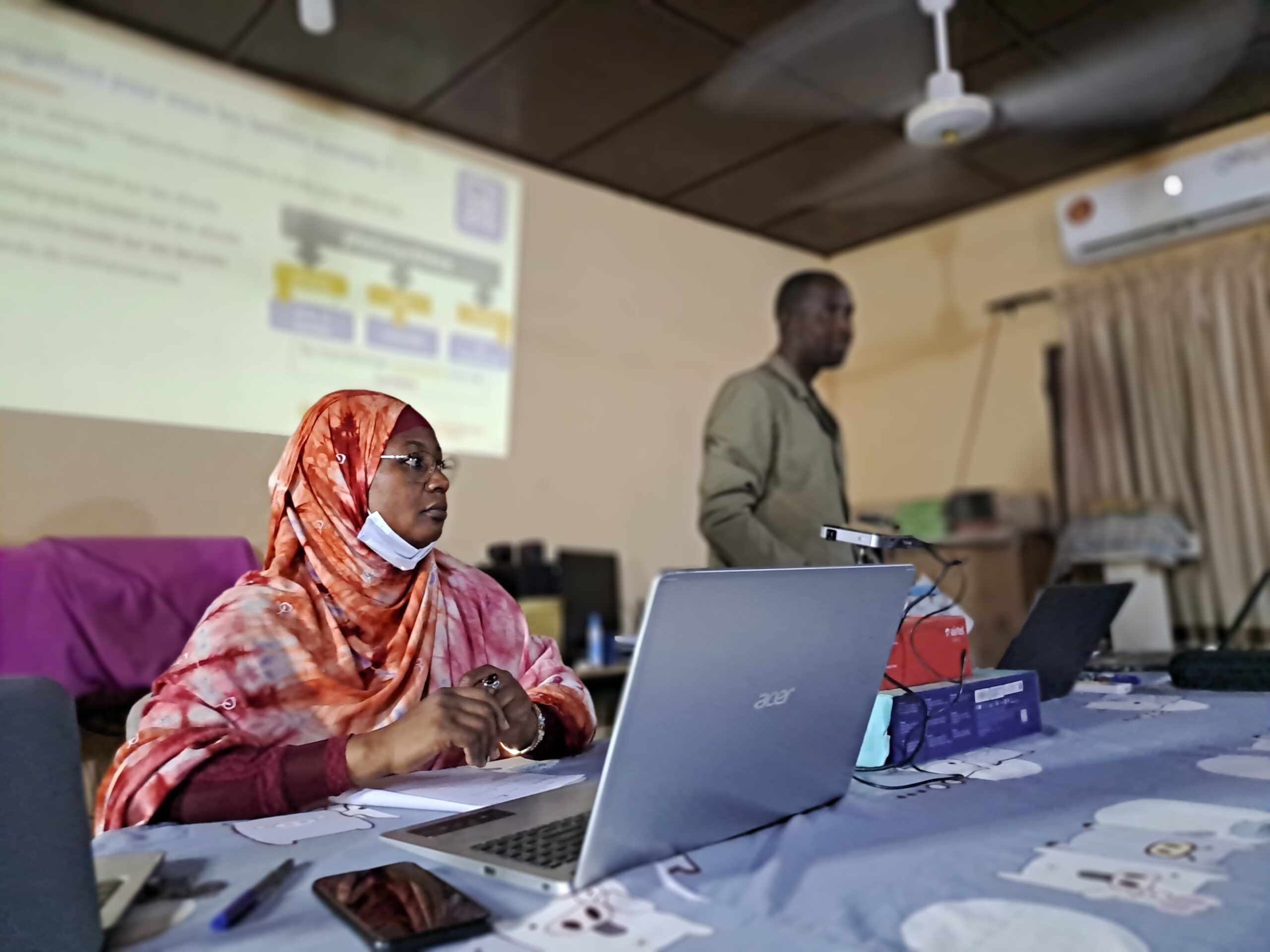 Woman at a computer with a man with a presentation in the background