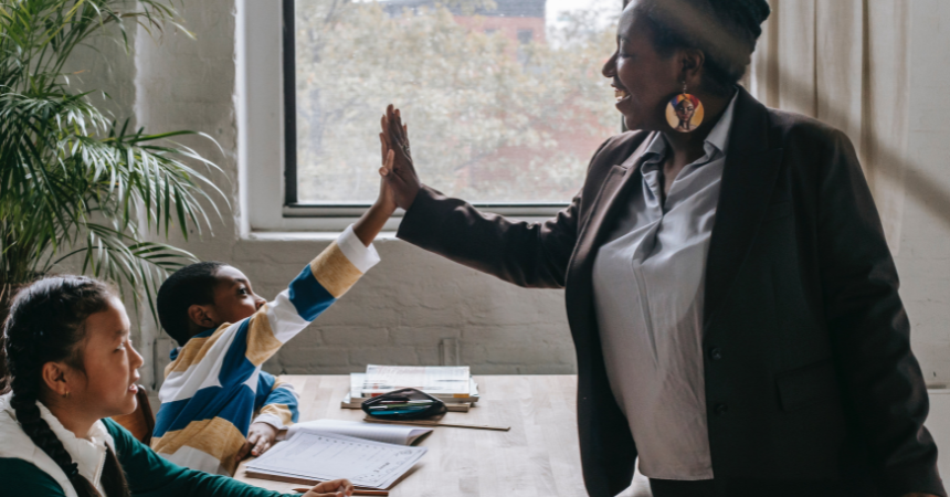 Teacher giving a high-five to a student as another student watches with a smile