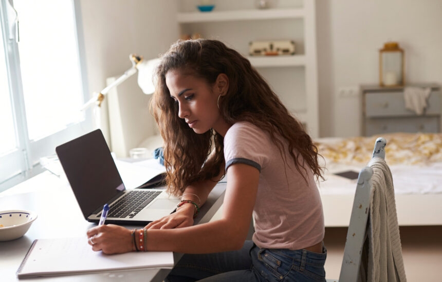 A woman works with a laptop and writes on a notepad