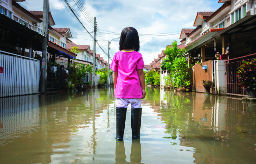 A girl stands in a flooded road watching her village