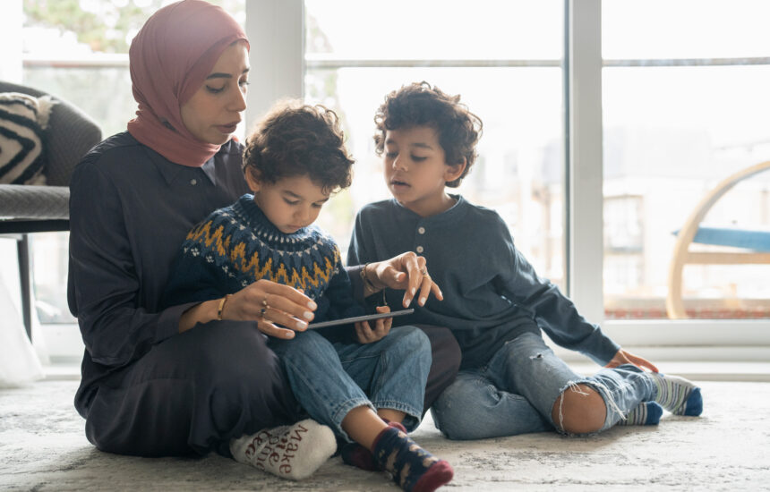 A woman helps two boys use a tablet