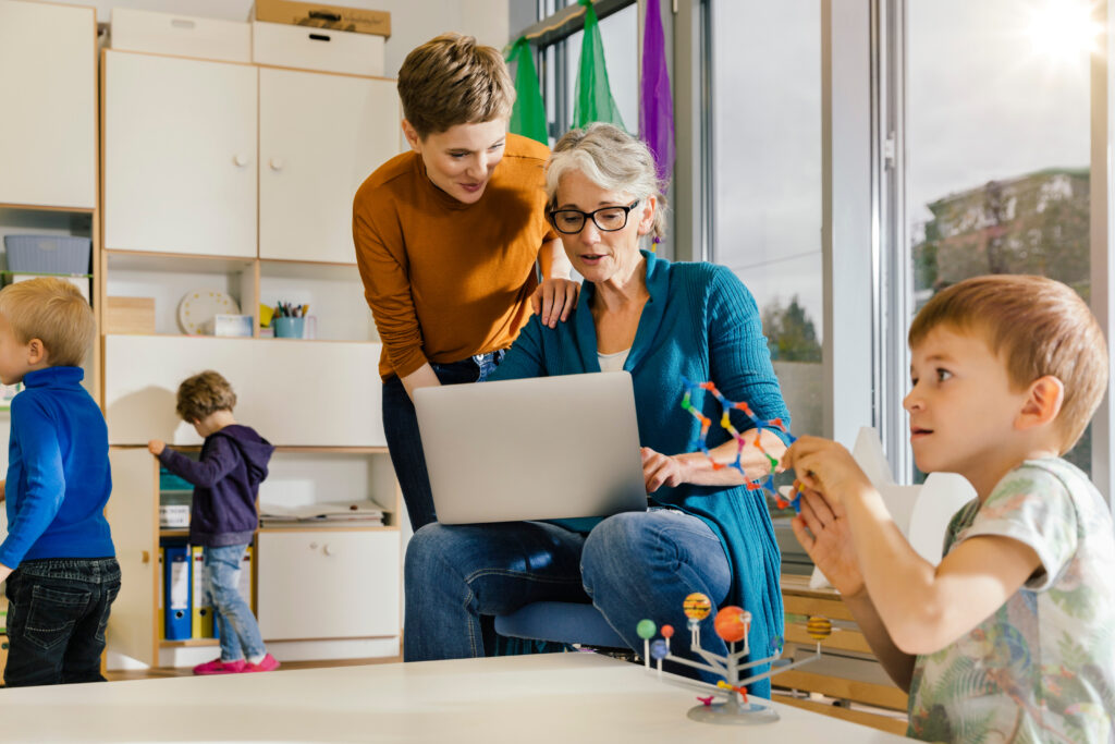 Pre-school teachers with laptop talking in kindergarten