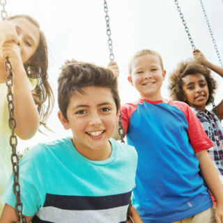 Five children happily playing together on a swingset outdoors