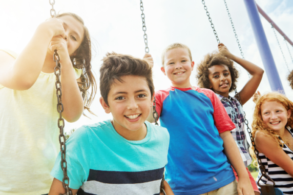 Five children happily playing together on a swingset outdoors