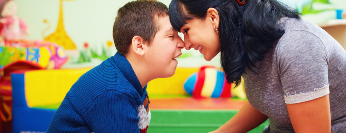 An adult and a child with a disability happily touching foreheads.