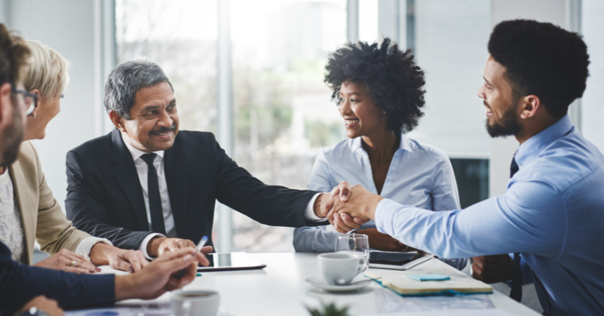 Three people happily shaking hands around a table.