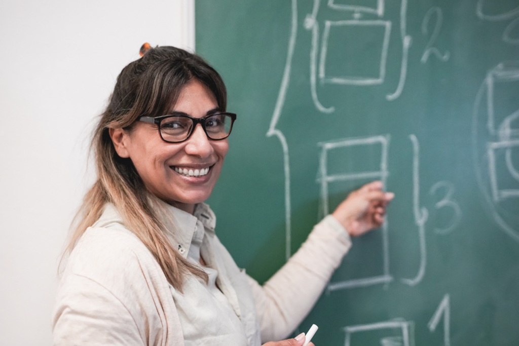 A happy teacher standing next to a chalkboard.
